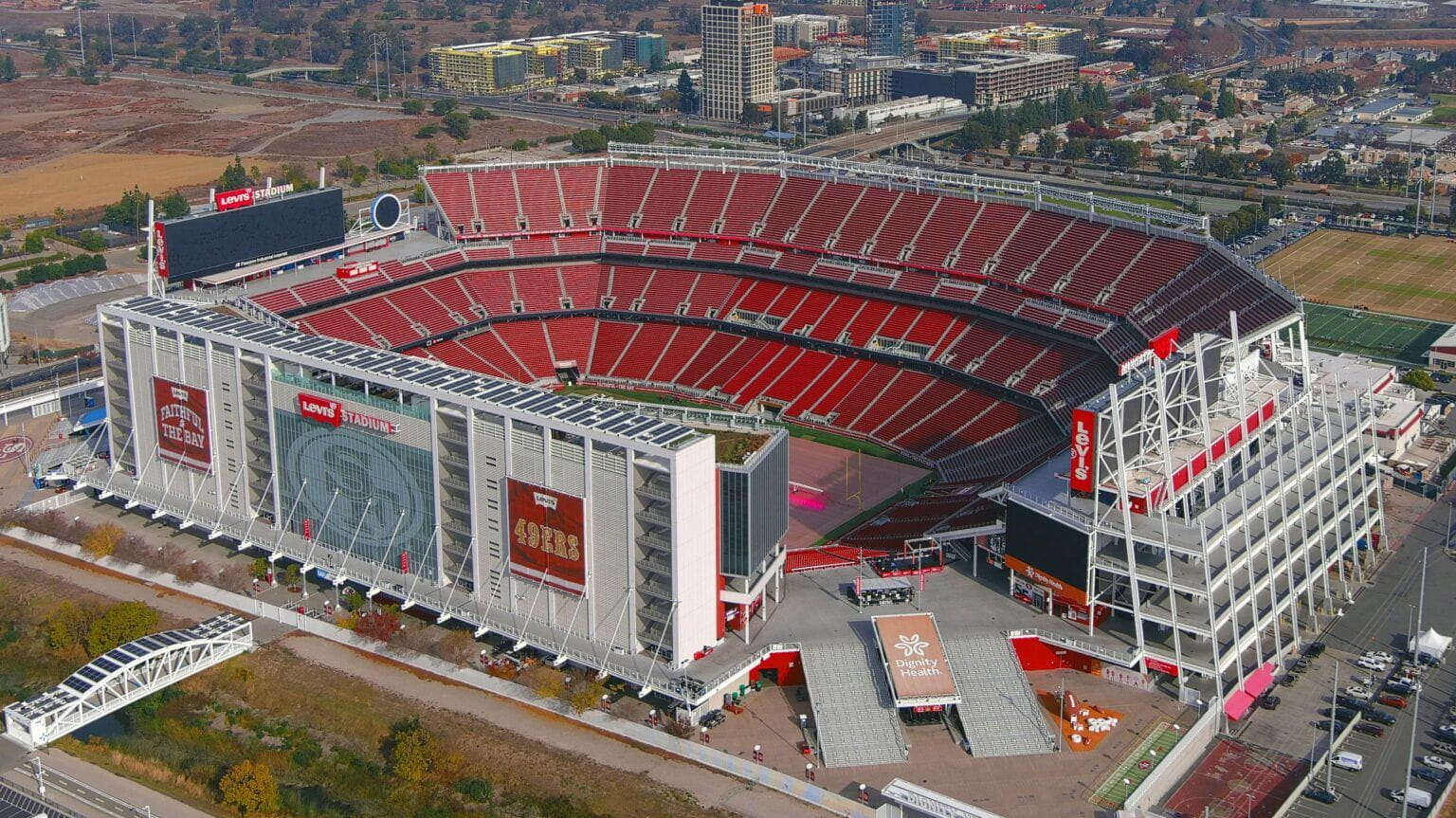 Aerial view of Levi’s Stadium with red seating and surrounding buildings. 