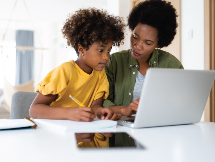 A school-aged child holding a pencil while looking at a laptop screen with an adult next to her.