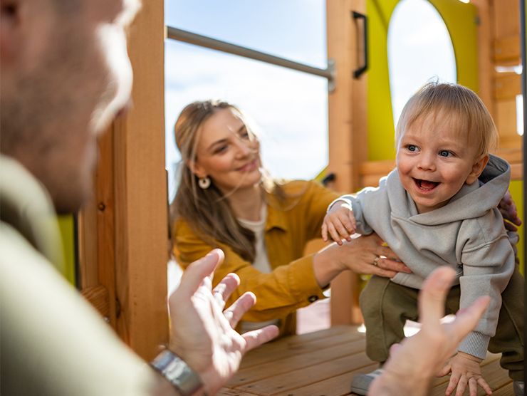A toddler boy on a play structure with mom and dad