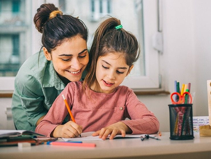A girl writing on a piece of paper while mom looks over her shoulder.