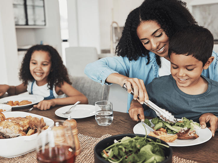 A woman helping a young boy plate food, while a young girl sits beside them at the dinner table