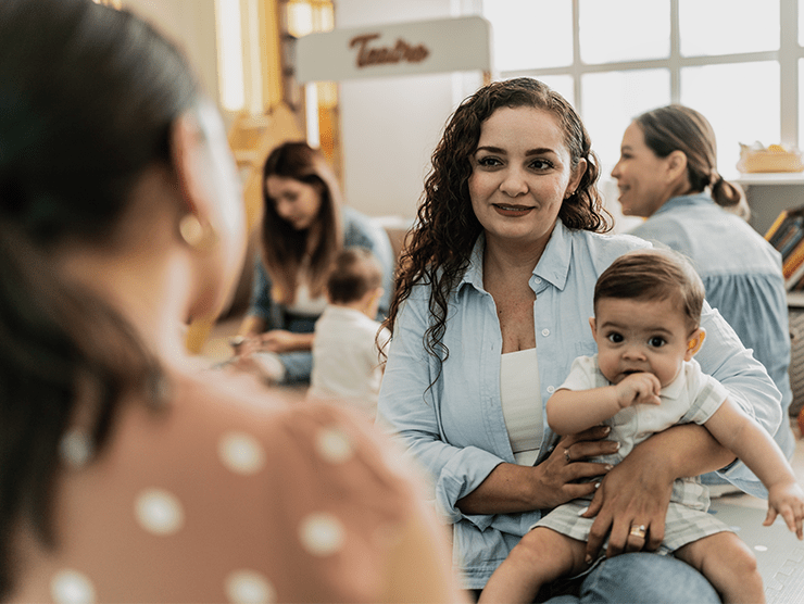 Mom holding her baby while talking to another woman in a classroom setting. 