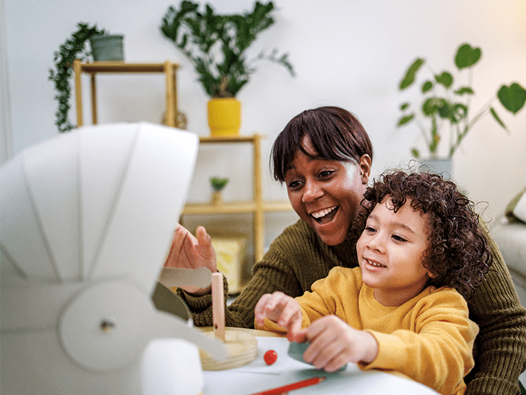 A young boy sitting with his mother while playing with a toy.
