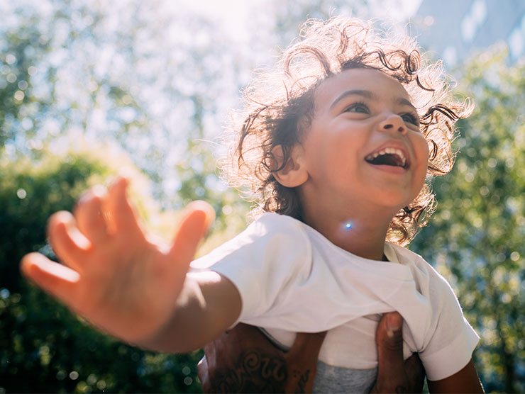 A young boy smiling while being lifted outdoors