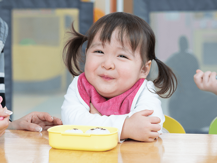 Toddler child smiling at camera with a lunchbox in front of her