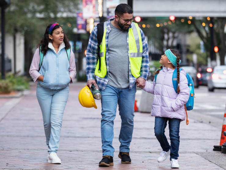 A dad in work uniform walking his two children to school.