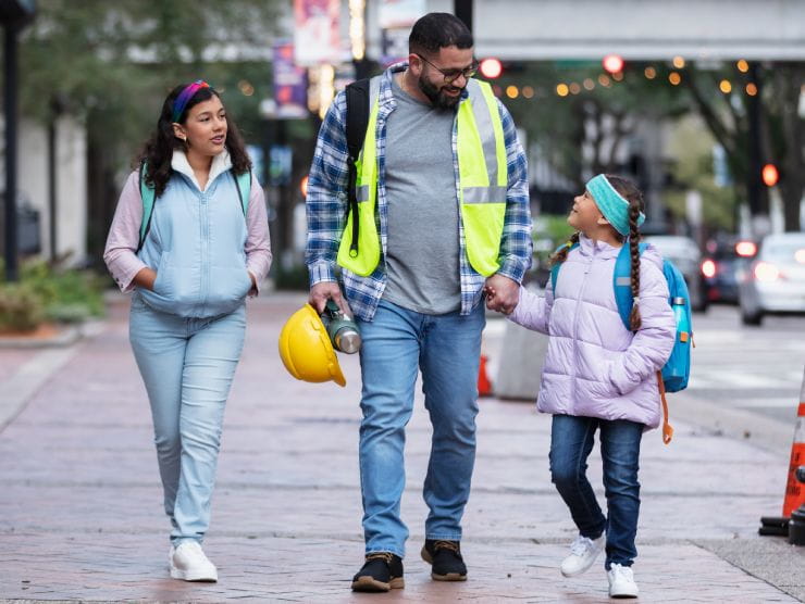 A dad in work uniform walking his two children to school.