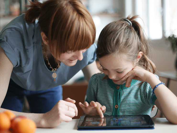 A young child playing on her ipad while mom looks over her shoulder