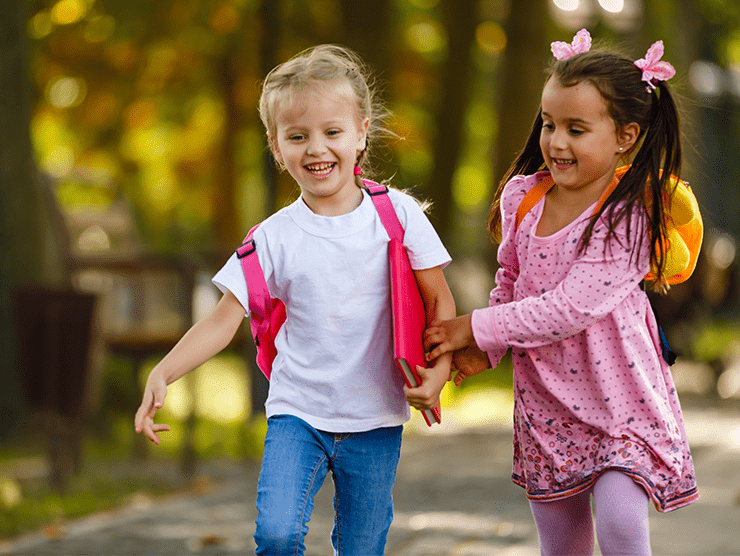 Two young girls with backpacks on walking outdoors