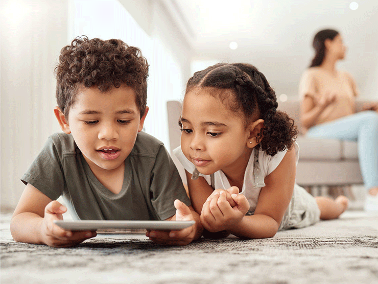 A young boy and girl laying on the floor looking at an ipad screen.