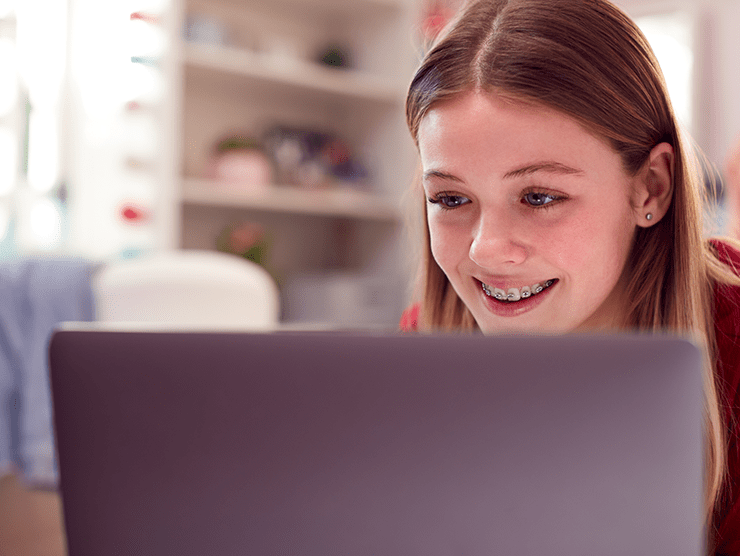 A teenage girl smiling while looking at her laptop screen.