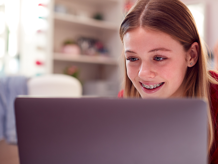 A teenage girl smiling while looking at her laptop screen.