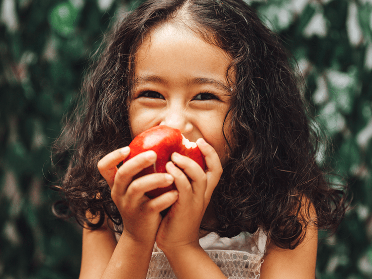 A young girl biting an apple with a big smile