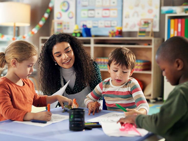 Three preschoolers sitting with a teacher in a classroom doing activities. 