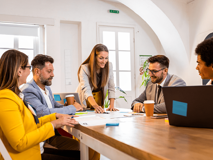 A woman pointing at a paper while her colleagues are listening to her.