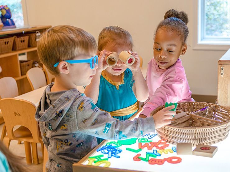 Three children exploring with materials on a light table in a Bright Horizons classroom.