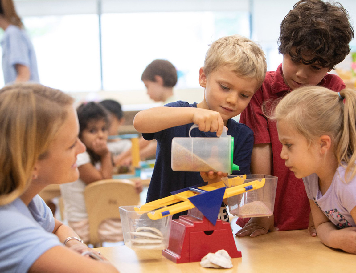 Three preschoolers doing an experience in class with their teacher.
