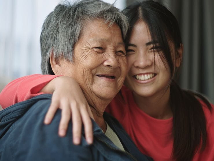 Smiling young woman with her arm around her smiling older parent.