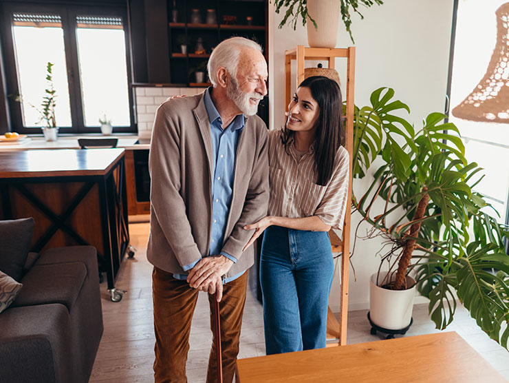 A woman walking with an elderly male across the living room.
