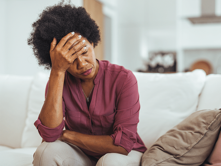 A woman sitting on couch while touching her head.