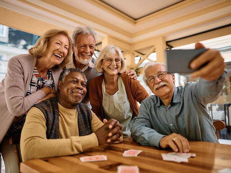 Three senior men and two senior women posing for a selfie around a table.