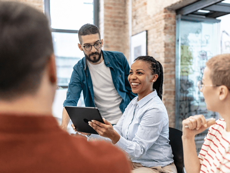 A woman holding an ipad in an office setting, talking to a team of people