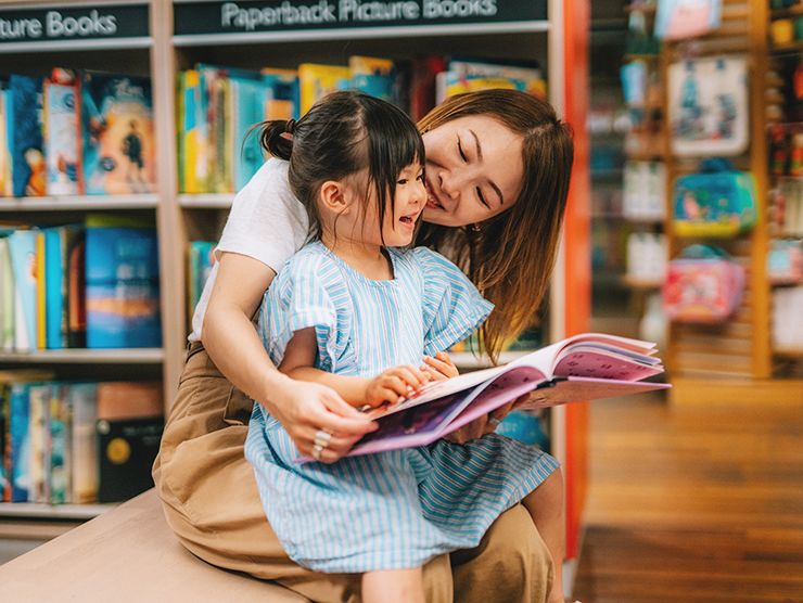 Young girl sitting on her caregiver's lap, reading a book in a bookstore.