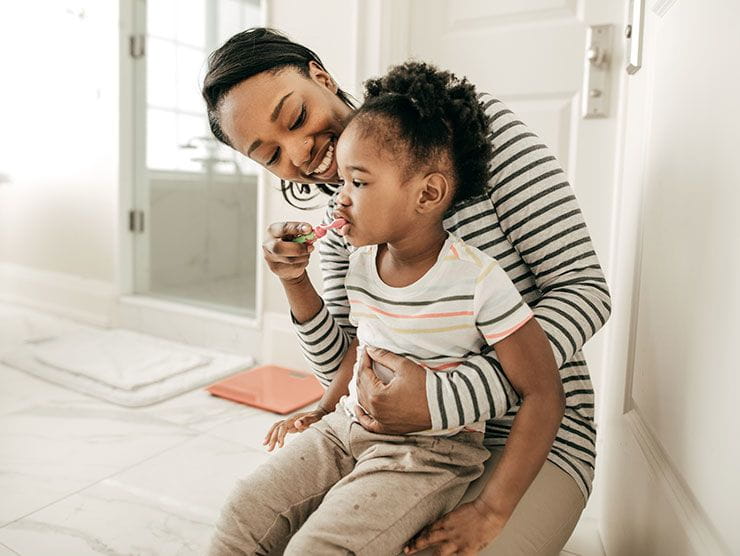 A mom holder her toddler child while helping her brush her teeth. 