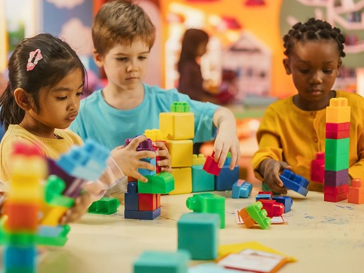Three preschool children sitting at a table building with Lego blocks.