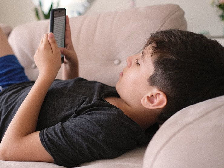 A boy lying on a couch looking at a smartphone.