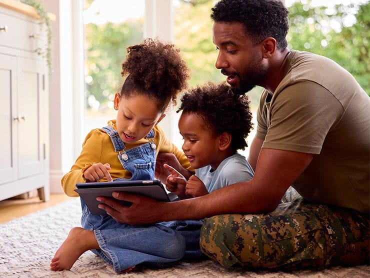 A military father with his two young children looking at a screen.
