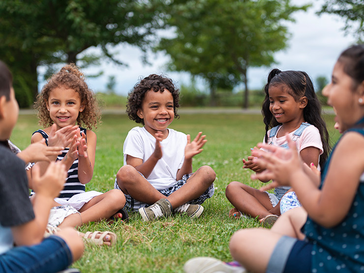 Diverse group of children clapping their hands while sitting on grass
