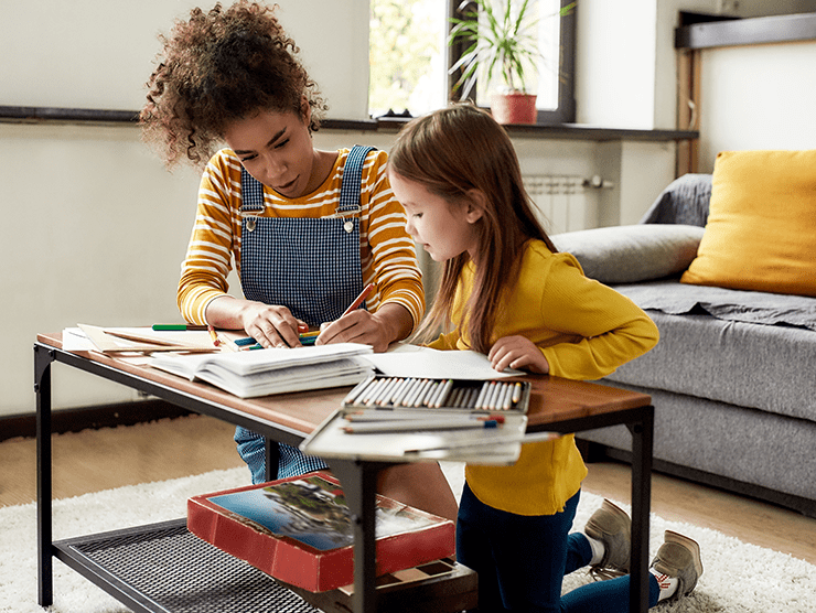 A young woman helping a school-age girl do her homework.