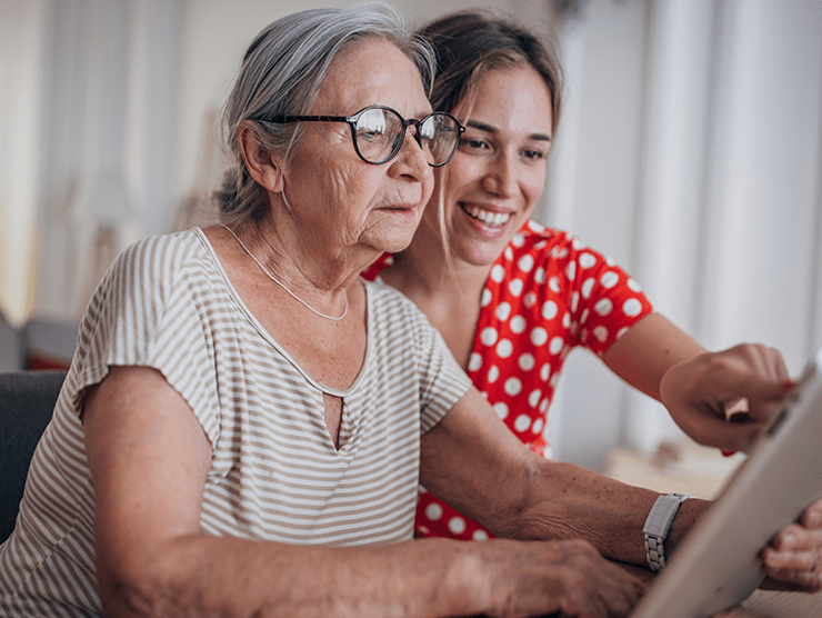 An elderly woman sitting next to her daughter looking at an ipad screen