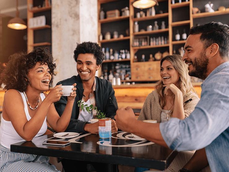A group of young adults sitting at a table in a cafe, laughing and talking