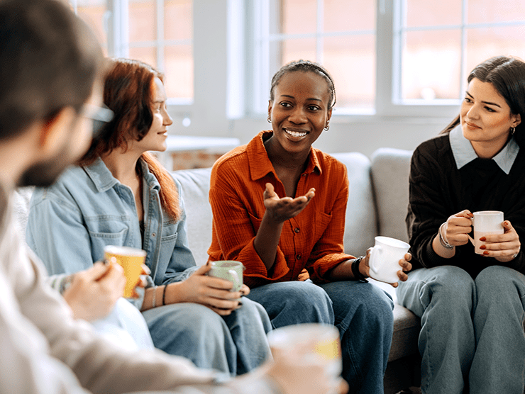 A group of young adults sitting together with a cup in their hands, talking. 