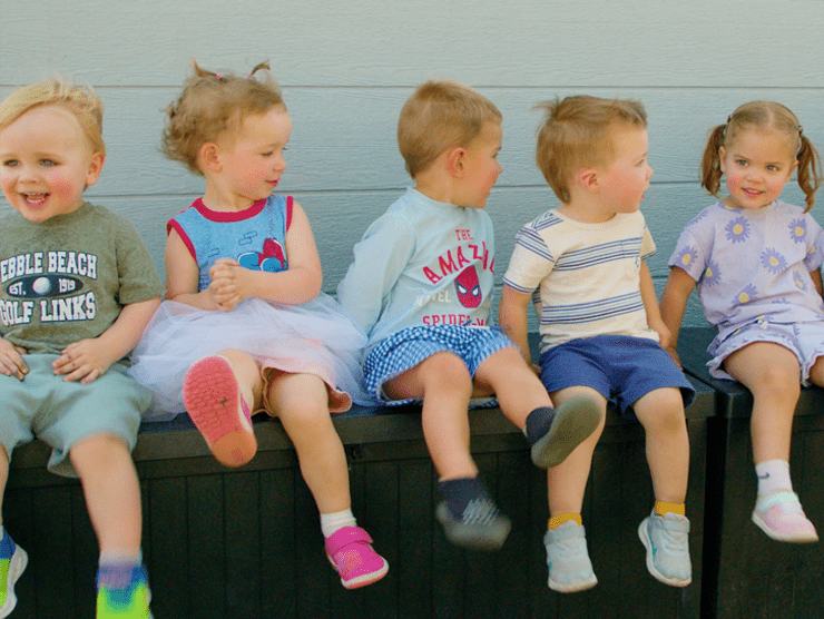 5 preschool children sitting on a bench with smiles on their faces.