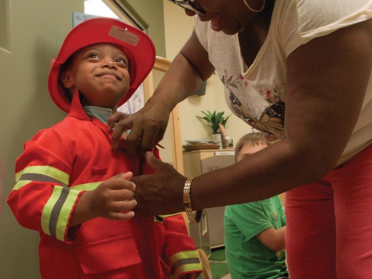 A woman helps a young boy button his firefighter outfit.