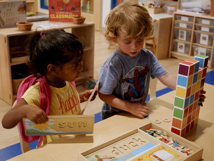 A young girl and a young boy in a classroom setting, playing with blocks