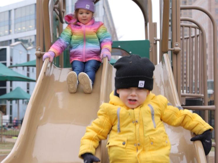 Two young children playing on a playground slide.