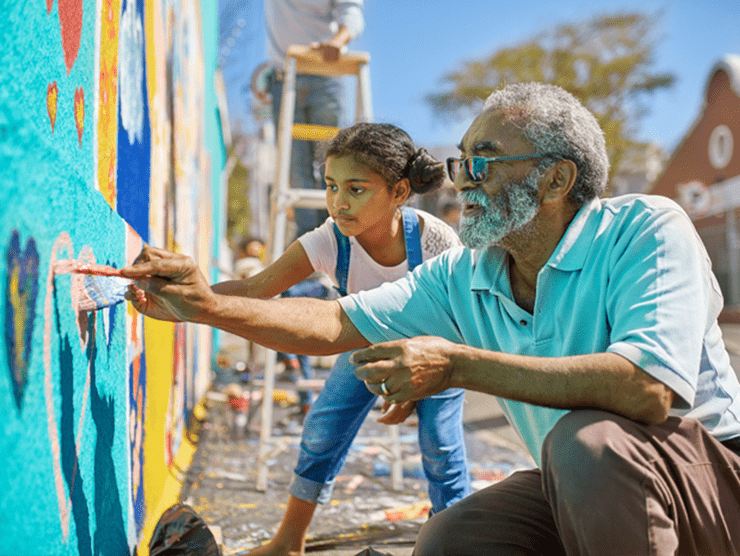 An older man with a child painting a wall in their community
