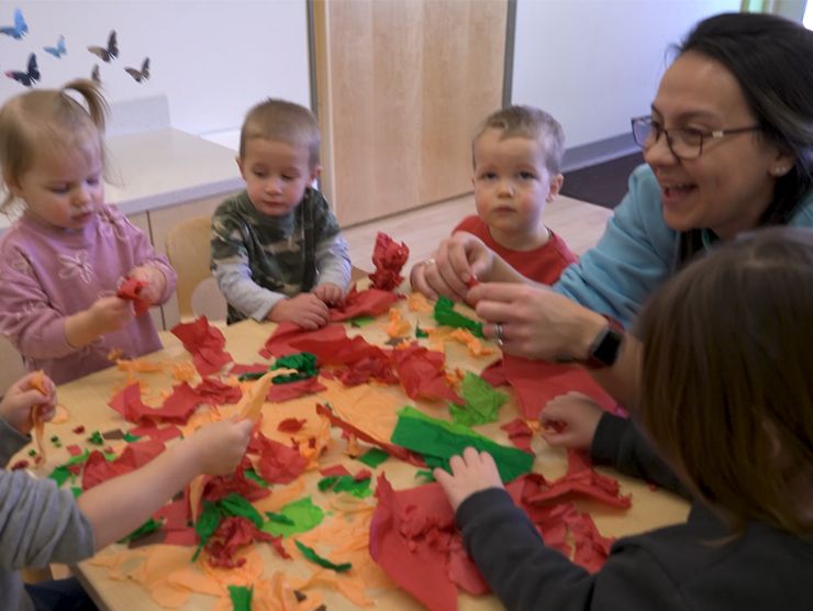A teacher sitting at a table with preschoolers crumbling tissue paper