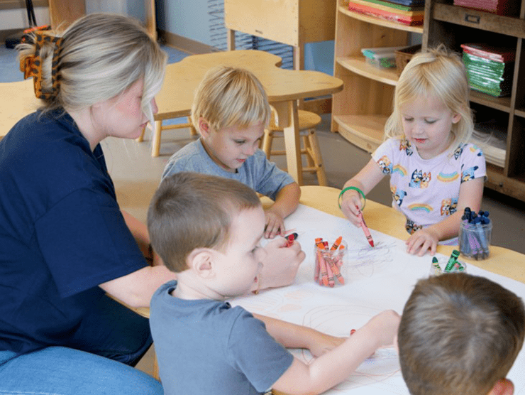 Teacher sitting with preschool children around a table painting. 
