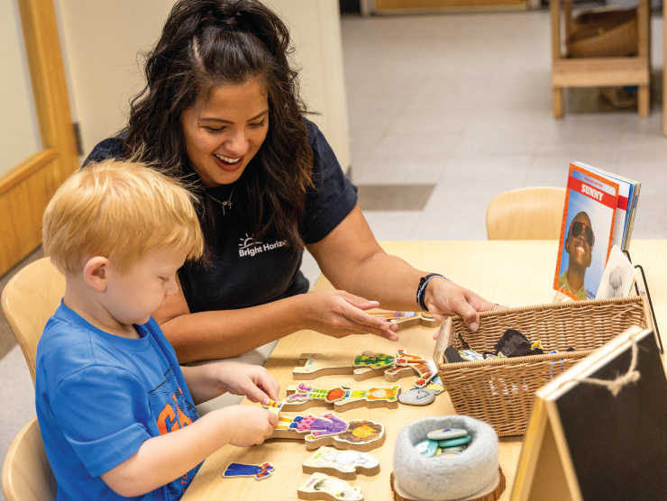 A young child solving a puzzle with a teacher next to him in a classroom setting