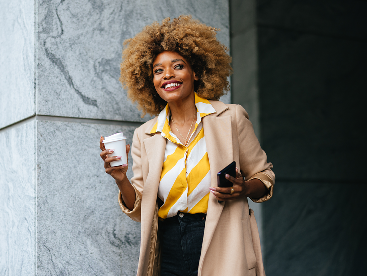 An adult professional holding cup of coffee and phone outdoors.