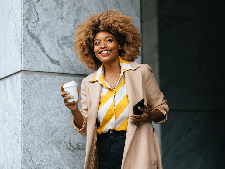 An adult professional holding cup of coffee and phone outdoors.