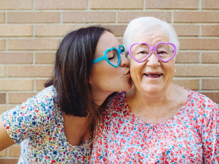 An adult woman kissing her elderly mother on the cheek.