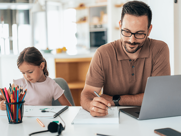 Working dad with a laptop sitting next to his child at home. 