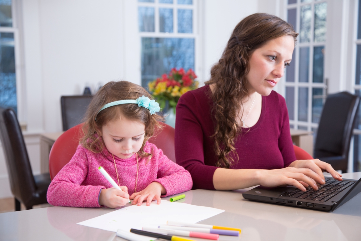 Mother working at home with child beside her