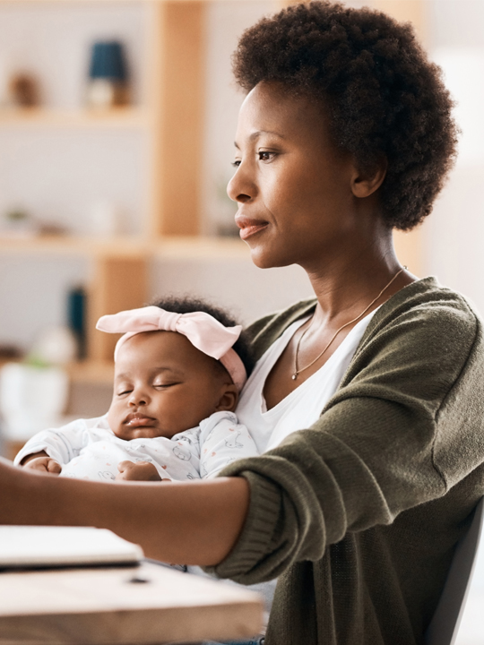 mother doing work at desk with sleeping daughter in lap